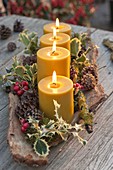 4 yellow candles in bark, decorated with ilex, red berries