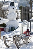 Snowy garden with snowman and sled with lanterns