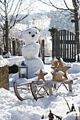 Snowy garden with snowman and sleigh with wooden stars
