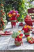 Fiery table decoration with vegetables and summer flowers in red cups