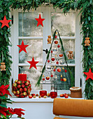 Weihnachtlich geschmücktes Fenster mit Äpfeln, Sternen und Girlande aus Zweigen