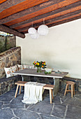 Tisch mit Bank auf überdachter Terrasse mit Natursteinboden