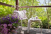 Vintage-style crockery on ornate metal table and cushion on chair on wooden deck