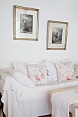 Vintage-style cushions on white loose-covered sofa below framed black and white photos
