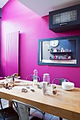 Baking utensils on wooden table in front of black-framed mirror on magenta wall