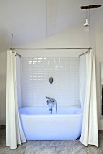 White bathtub with shower curtain bathed in blue light in renovated period building