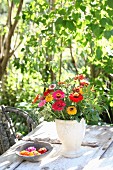 Zinnias, grasses and branches of dog rose in simple vase on garden table