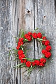 Wreath of red zinnias and switchgrass hung from board wall