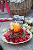 Candle in arrangement of rose hips and Virginia creeper leaves