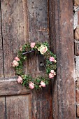 Romantischer Blütenkranz mit rosafarbenen Rosenblüten und Efeublättern an Türdrücker