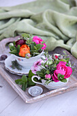 Colourful flower arrangements in old-fashioned teacups on vintage wooden tray