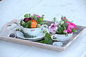 Colourful flower arrangements in old-fashioned teacups on wooden tray