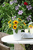 Sunflowers and ornamental grasses in jug on garden table