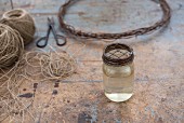 Jar of water with metal lid in front of parcel string and wire wreath