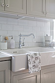 Tea towel draped over large ceramic sink in country-house kitchen with grey cabinets