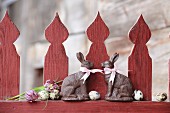 Two chocolate bunnies with pink ribbons on red picket fence