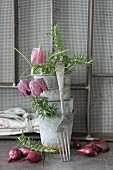 Vintage-style arrangement of stacked zinc pots, snake's head fritillaries, onions and fork