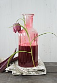 Snake's head fritillary leant against vintage carafe of red drink