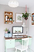 Monitor on mint-green retro desk and white wooden chair in corner
