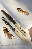 White linen napkins embroidered with birds' feathers and vintage-style cutlery