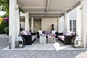 Comfortable black rattan sofas with mauve cushions and scatter cushions on roofed terrace