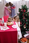 Kleines Mädchen vor geschmücktem Weihnachtsbaum auf eine Etagere voller Plätzchen blickend
