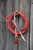 Wreath of twigs with posy of rose hips hung from red and white ribbon on rustic board wall