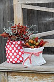 Autumn arrangements of rose hips and autumn leaves in pots wrapped in gift wrap on vintage wooden bench