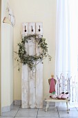 Wreath of hops hanging from coat pegs on vintage wooden boards next to angel figurine on stool