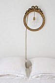Pendant lamp hung in round gilt frame above bed