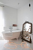 Rope light on floor next to free-standing bathtub and large mirror leant against wall in bathroom