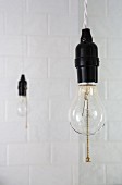 Two lightbulbs hanging in front of white tiles
