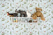 Vintage-style toys on shelves mounted on floral wallpaper