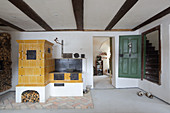 Alter gelber Kachelofen und Küchenofen neben Tür zur Treppe