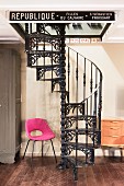 Pink retro chair next to black cast iron spiral staircase