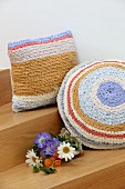 Flowers next to pastel cushions with crocheted covers made from T-shirt yarn