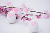 Rosafarbene Blütenzweige und weiße Eier mit Herz-Motiven