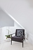 Black armchair with patterned scatter cushion under sloping ceiling