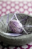 Easter egg painted purple, feathers and delicate cord in stone dish