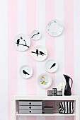 Decorative wall plate painted with bird silhouette on striped wallpaper