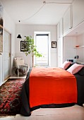 Red blanket on bed surrounded by fitted cabinets