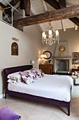 Bed with purple frame below exposed roof beams in bedroom