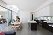 Offene Designerküche mit Essbereich und Blick durch geöffnete Glasschiebetür in Wohnbereich