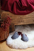 Grey felt slippers on white sheepskin rug under rustic wooden bed