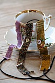 Three hand-woven bracelets with glass beading draped over gold-rimmed teacup