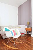 Classic, white rocking chair in front of bed and retro bedside table