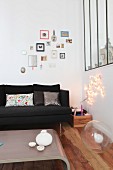 Gemütliche Zimmerecke mit schwarzer Couch vor Bildergalerie und Innenverglasung