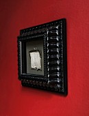 Elegante, silberfarbene Kettentasche in schwarzem Bidlerrahmen an roter Wand