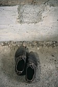 Pair of worn men's shoes next to concrete wall