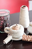DIY Gefilzte Tasse mit Milchhäubchen, Schokolade, Zuckerdose, Garn und Glasbehälter auf Tisch